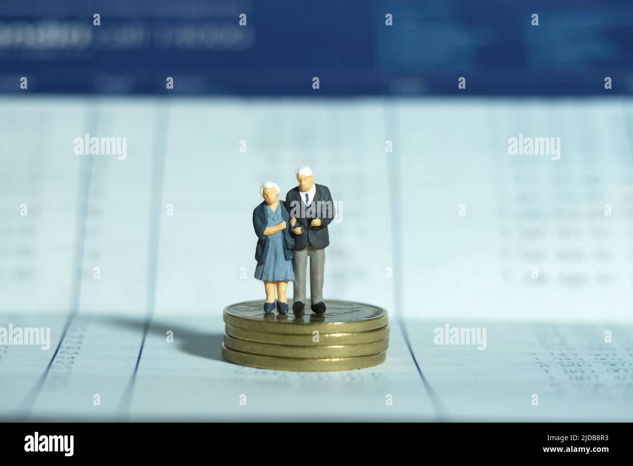 Miniatur Menschen Spielzeug konzeptuelle Fotografie. Ein älteres Paar, das über dem Münzstapel auf der geöffneten Buchbankkontoseite steht. Finanz- und Sparkonzept. Stockfoto