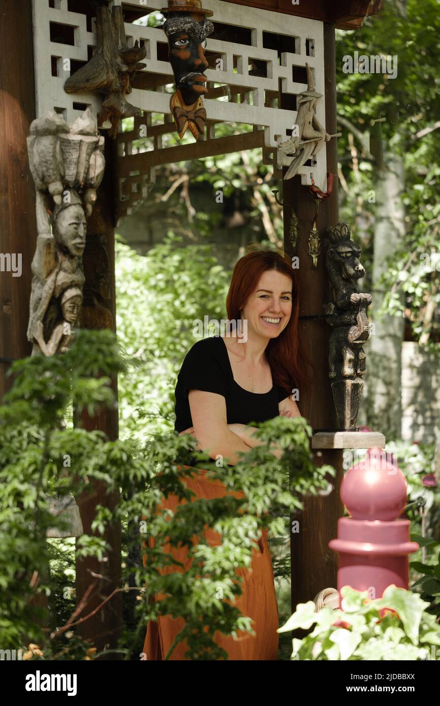 Frau in ihrem 40s Blick weg in grünen Garten in Pavillon. Ruhe haben, denken. Weibchen mit Ingwerhaar im Gartenhaus. Entspannung im Park im Sommer Stockfoto