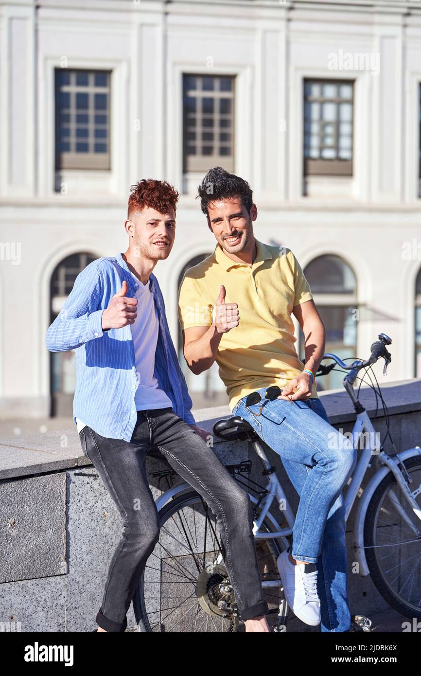 Junge schwule Paar mit einer Gay Pride Flagge, während ein Fahrrad im Freien fahren. LGBT, Beziehungs- und Gleichstellungskonzept. Stockfoto