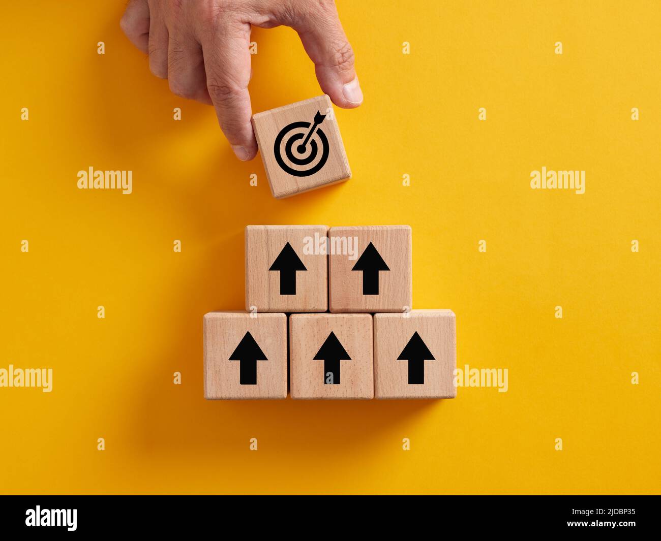 Hand platzieren eines Ziels über den Holzwürfeln mit Pfeil-Icons. Erreichen von Geschäftszielen, Zielsetzung und Geschäftsentwicklungskonzepten. Stockfoto