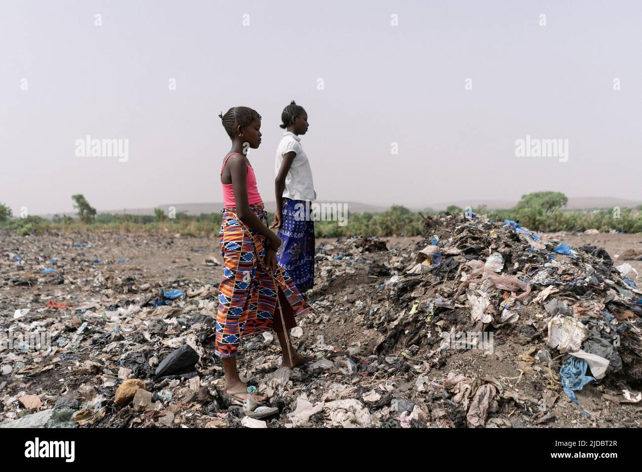 Zwei afrikanische Müllsammler-Mädchen machen eine Pause, stehen direkt, um ihre Schmerzen auszuruhen, während sie auf einer Deponie nach recycelbarem Material suchen Stockfoto
