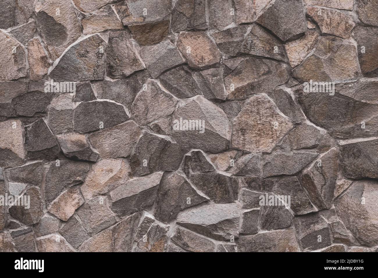 Abstraktes Muster aus braunem Stein. Backsteinmauer Hintergrund. Raue Granitoberfläche. Zerbrochener Fels. Dekorative Fliesen an der Fassade des Gebäudes. Stockfoto