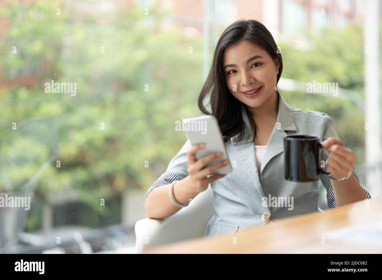 Lächelnde asiatische Geschäftsfrau, die im Büro telefoniert. Unternehmerin aus Kleinunternehmen, die ihr Mobiltelefon anschaut und lächelt. Stockfoto