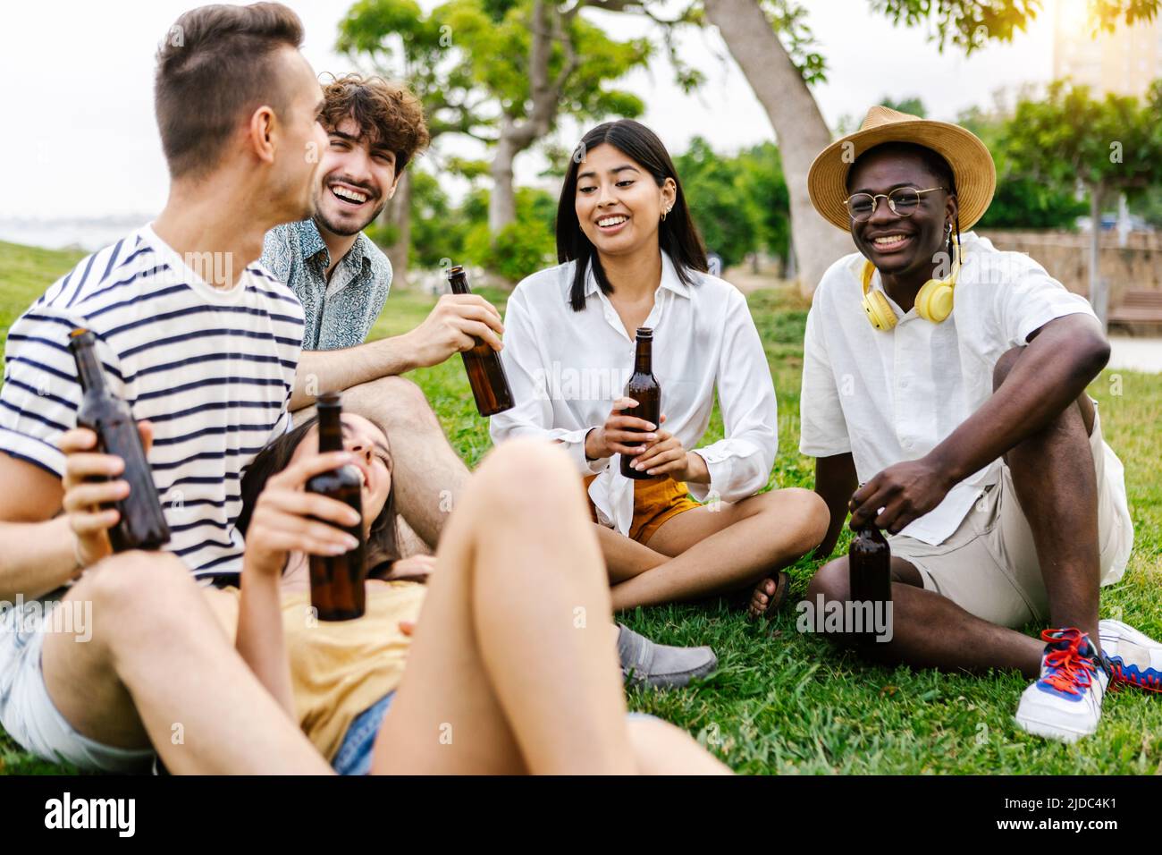 Junge Gruppe von verschiedenen besten Freunden, die sich im Stadtpark beim Biertrinken aufmachen Stockfoto