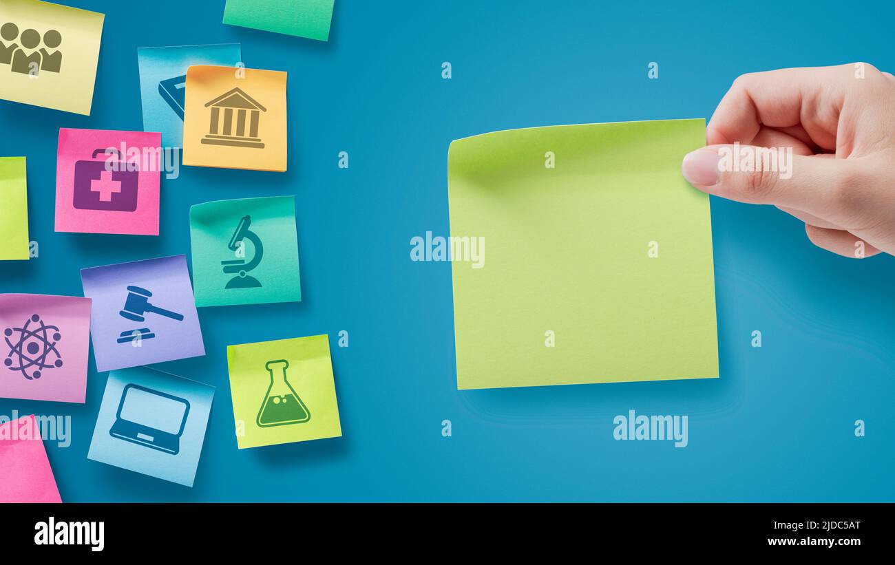 Haftnotizen mit Symbolen für Schulfächer hält ein Schüler eine Notiz mit leerem Kopierbereich Stockfoto