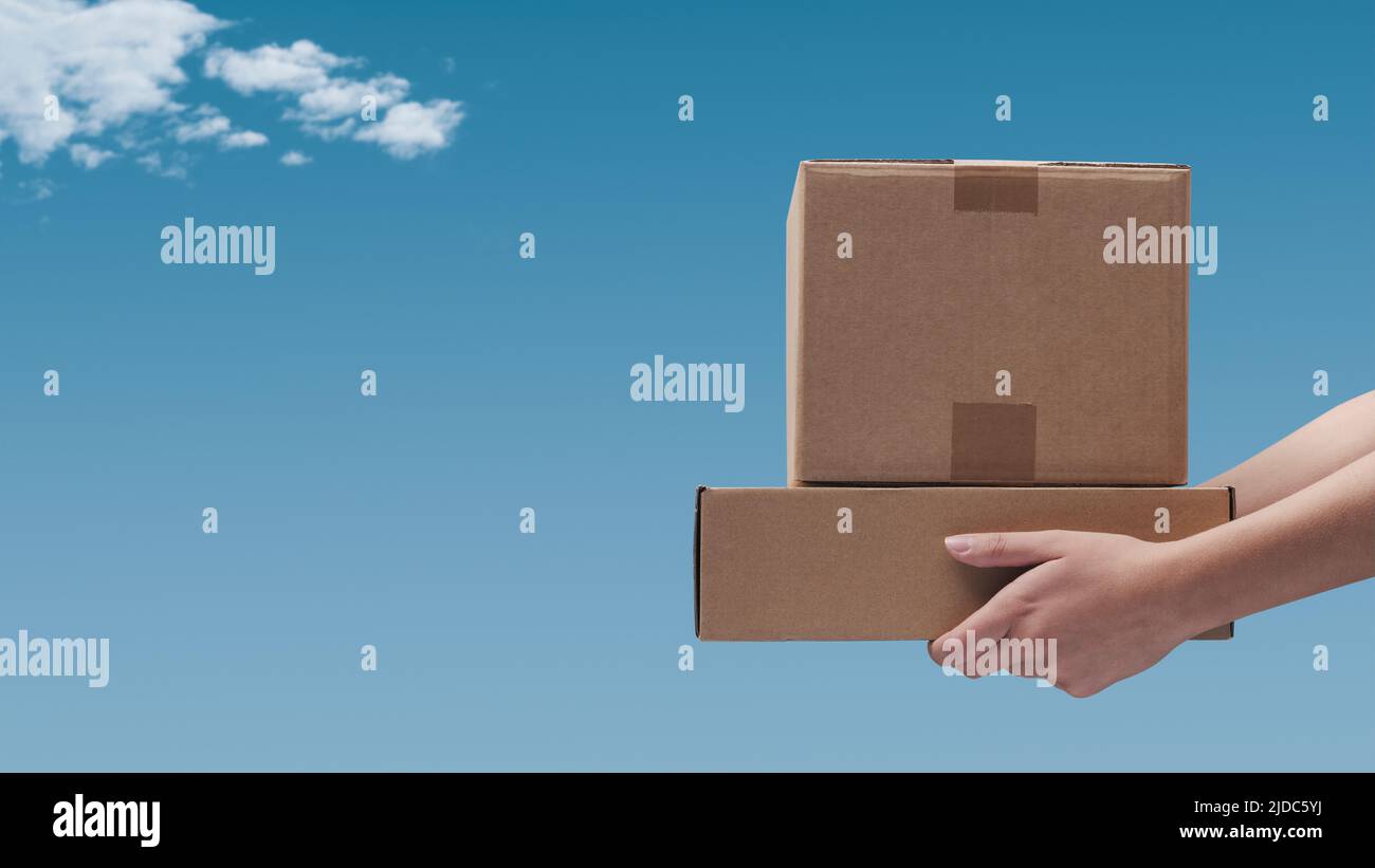 Hände mit Lieferkisten und blauem Himmel im Hintergrund: Liefer- und Versandkonzept Stockfoto