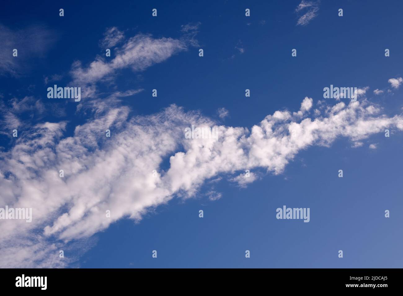 Weiße Wolken diagonal über dem Rahmen eines satten blauen Himmels. Stockfoto