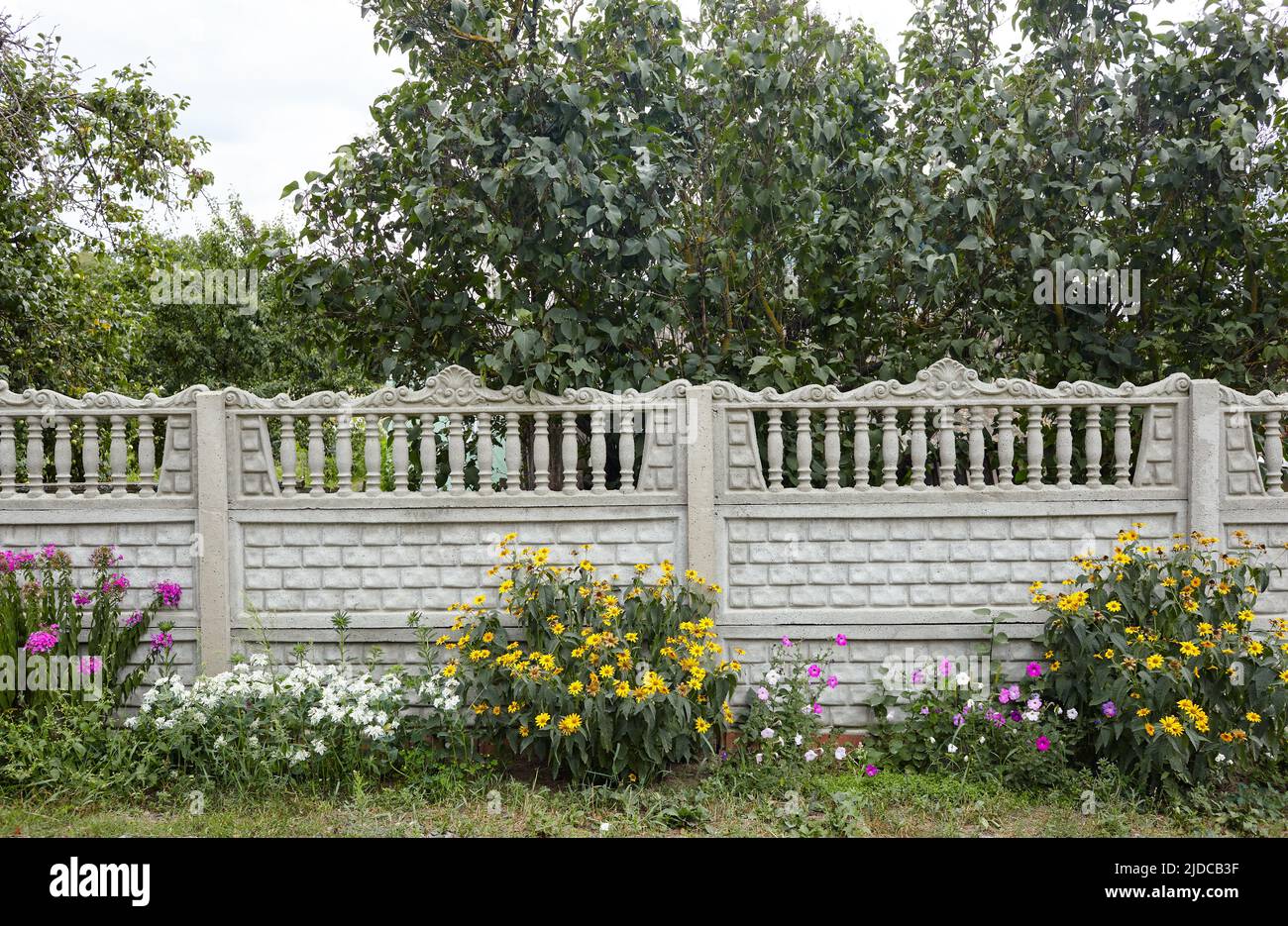 Eine alte klassische Balustrade im Freien mit Blumen. Antikähnlicher Steinzaun mit Säulen in der Nähe der europäischen Vorstadthütte Stockfoto