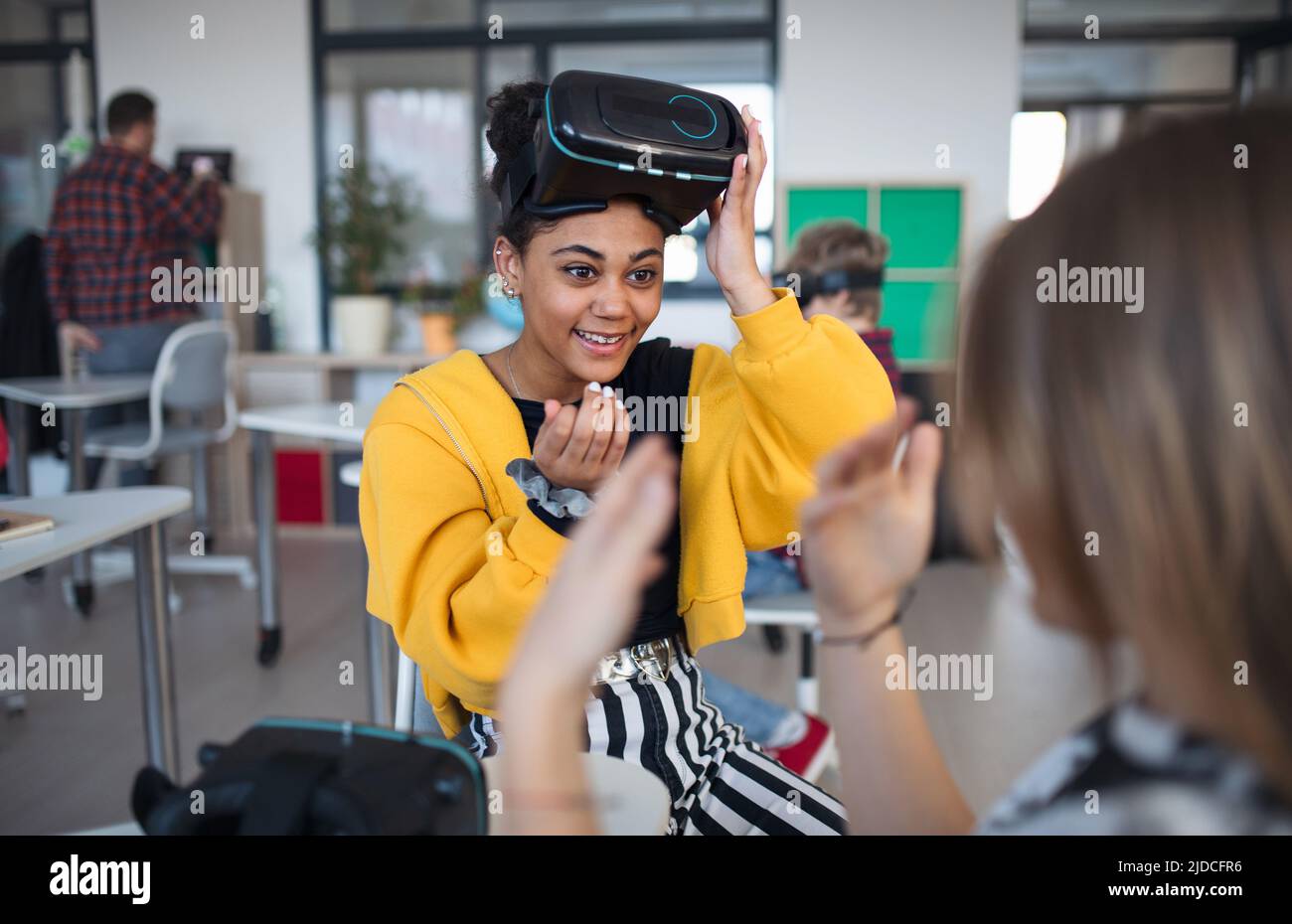 Glückliche Schülerin, die in der Schule im Informatikunterricht eine Virtual-Reality-Brille trägt und mit ihrem Schulkameraden spielt. Stockfoto
