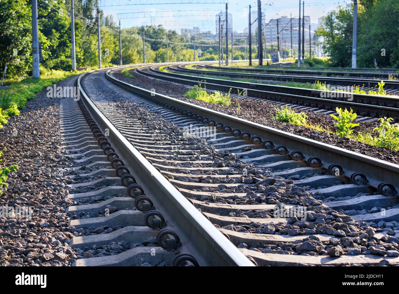 Nahaufnahme der Bahngleise einer mehrspurigen Eisenbahn, die sich in die Ferne vor dem Hintergrund einer Sommermorgendstadt am Horizont erstreckt. Stockfoto