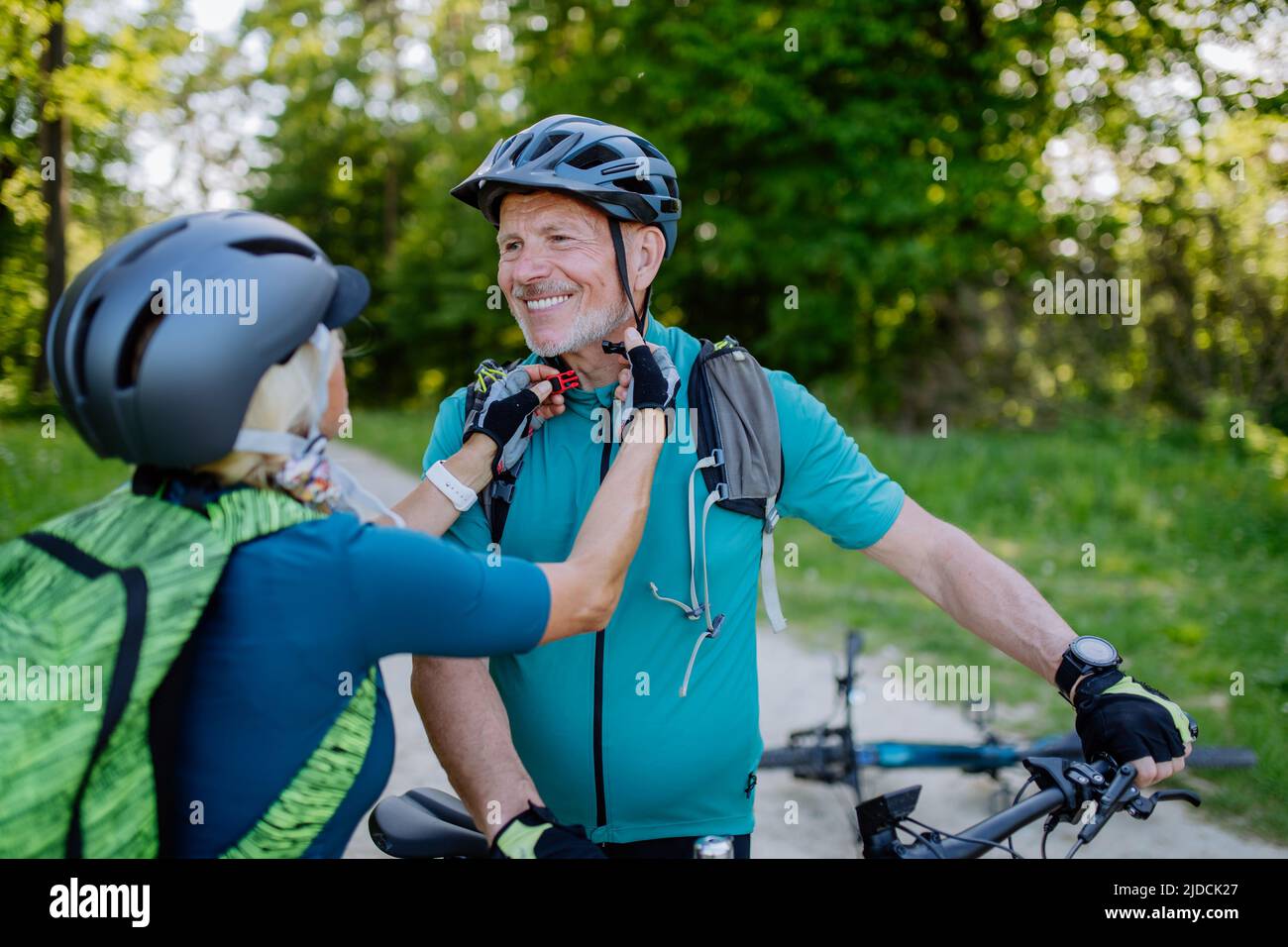 Aktives Seniorenpaar, das im Sommerpark Fahrrad fährt, Helm aufsetzt, gesundes Lifestyle-Konzept. Stockfoto
