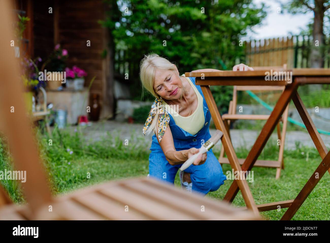 Ältere Frau putzt und renoviert Gartenmöbel und bereitet den Garten für den Sommer vor Stockfoto