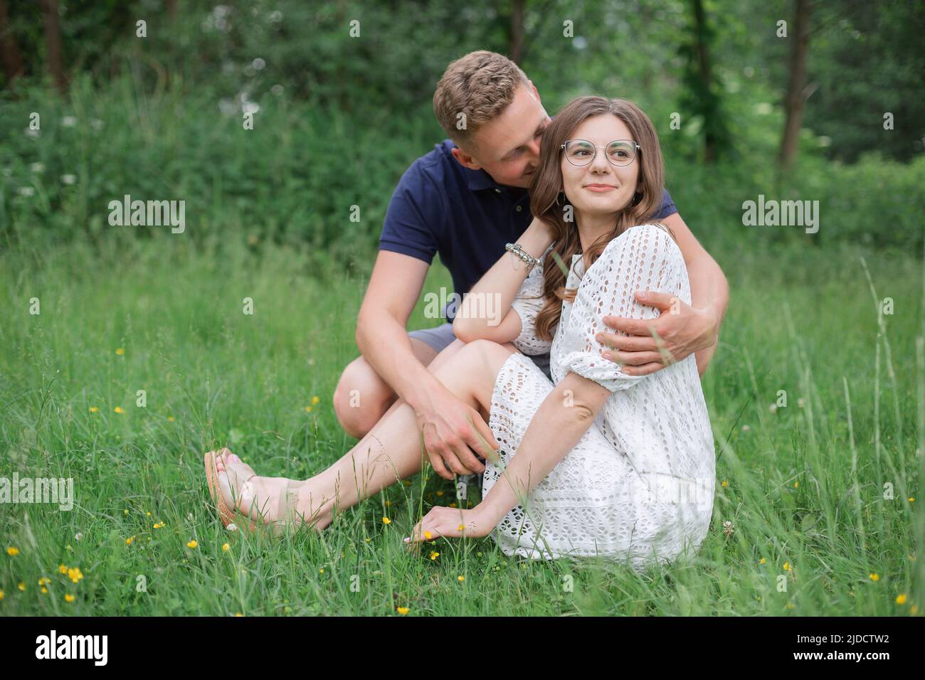 Liebevolles junges Paar, das im Park auf Gras sitzt und sich küsst. Junge Männer und Frauen genießen den Sommertag. Glückliche Menschen in der Liebe, Honigmond Stockfoto