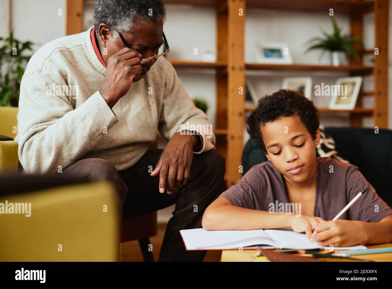 Ein afroamerikanischer Großvater sitzt zu Hause mit seinem Enkel und hilft ihm bei den Hausaufgaben. Nachhilfe zu Hause. Stockfoto