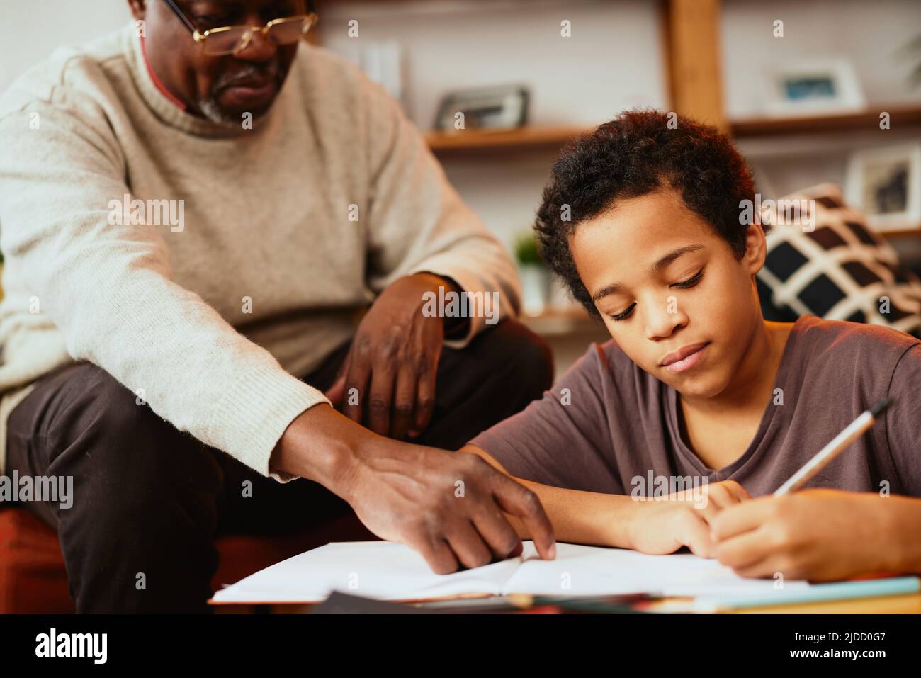 Intelligenter afrikanischer Junge, der seine mathematischen Hausaufgaben mit ein wenig Hilfe seines Opa macht. Nachhilfe und Bildung Stockfoto