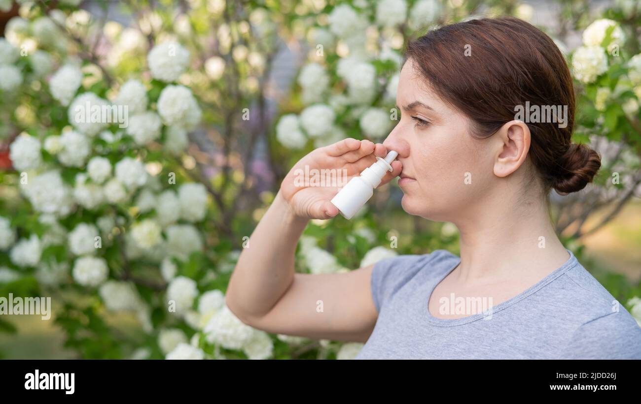 Kaukasische Frau verwendet ein Nasenspray, während sie im Park spazieren geht. Stockfoto