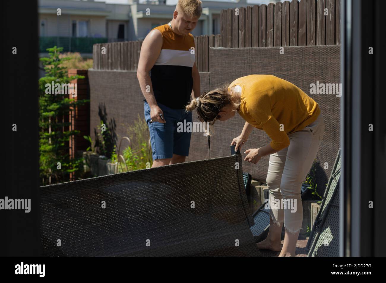 Frau, die Möbel zusammenstellt, während der Mann steht und ihre Arbeit anschaut. Paar Umzug in neue Heimat, Möbel Sofa für Terrasse Stockfoto