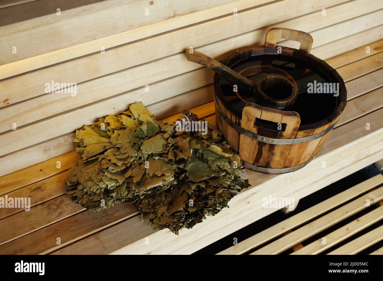 Saunaeimer voller Wasser mit Schöpfkelle und Besen auf der Holzbank