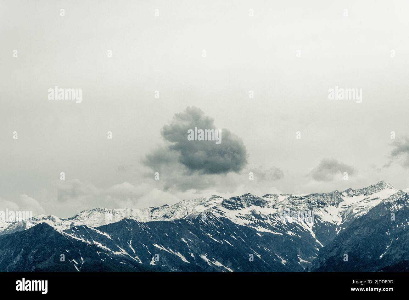 Einzelne dunkle Wolke gegen klaren Himmel, abstrakte Fotografie, Konzept, einzelne einsame Wolke über Schneespitzen Berg. Stockfoto