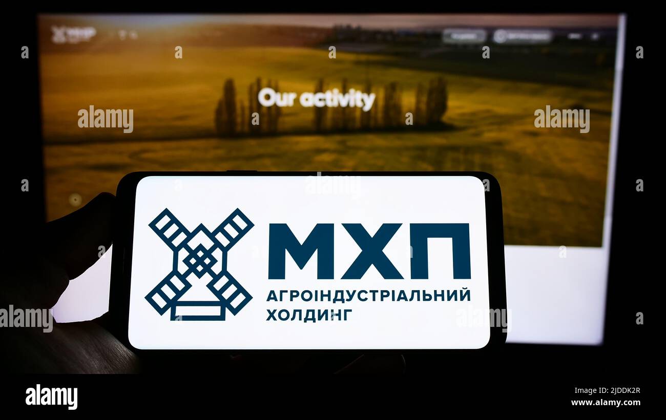 Person, die das Mobiltelefon mit dem Logo der ukrainischen Firma Myronivsky Hliboproduct (MHP) auf dem Bildschirm vor der Webseite hält. Konzentrieren Sie sich auf die Telefonanzeige. Stockfoto