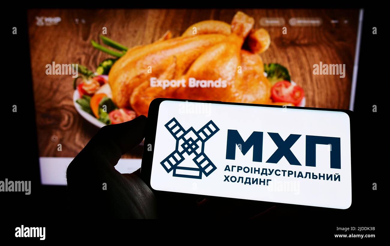 Person, die Mobiltelefon mit dem Logo der ukrainischen Firma Myronivsky Hliboproduct (MHP) auf dem Bildschirm vor der Webseite hält. Konzentrieren Sie sich auf die Telefonanzeige. Stockfoto