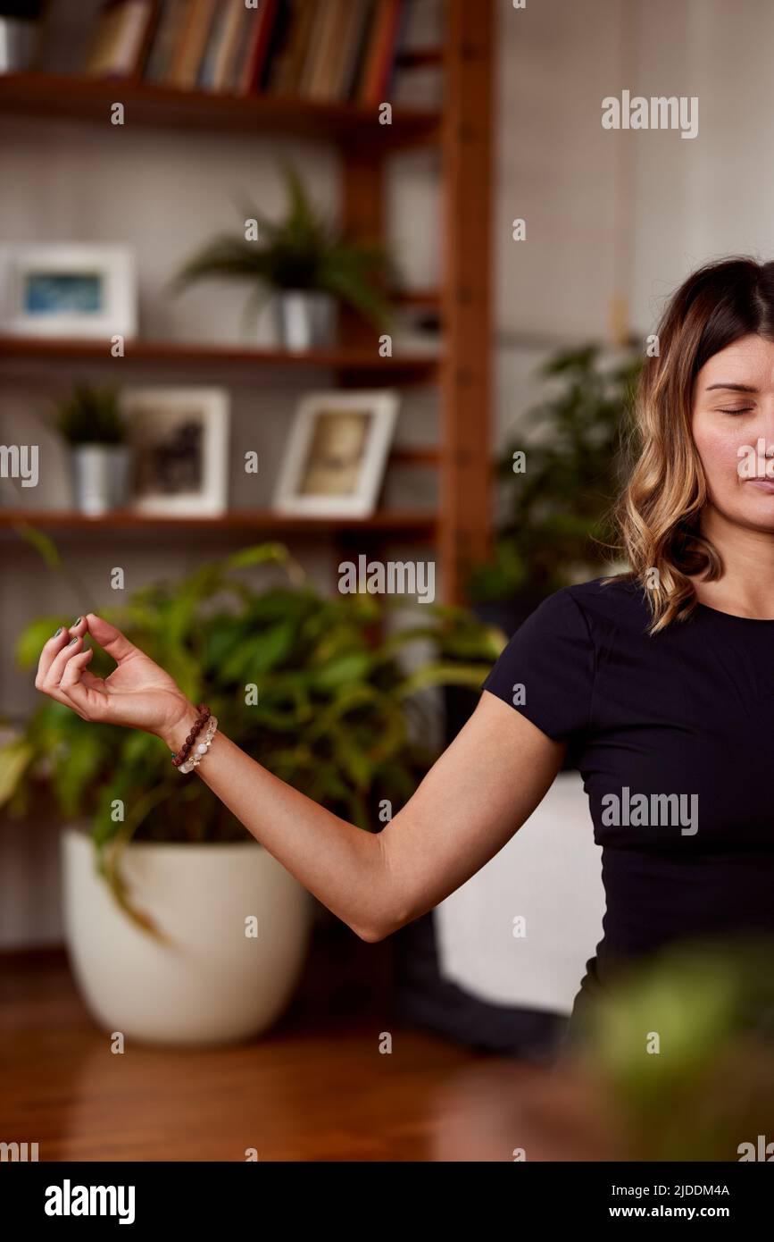 Eine ruhige Yogi-Frau mittleren Alters, die auf einer Yogamatte in einer Lotushaltung sitzt und meditiert. Eine Yogi-Frau, die zu Hause meditiert, übt zu Hause. Stockfoto