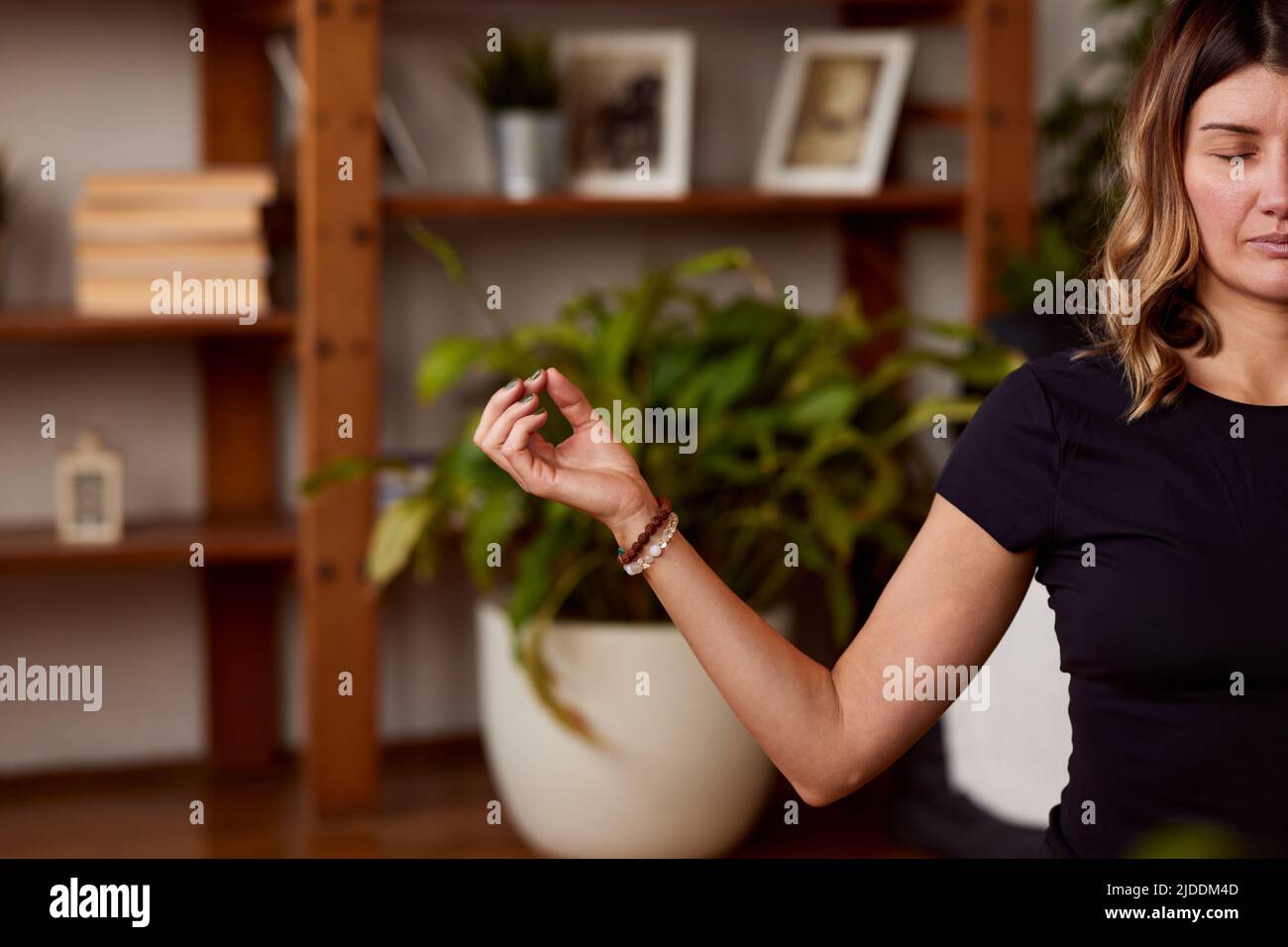 Eine ruhige Yogi-Frau mittleren Alters, die auf einer Yogamatte in einer Lotushaltung sitzt und meditiert. Eine Yogi-Frau, die zu Hause meditiert, übt zu Hause. Stockfoto