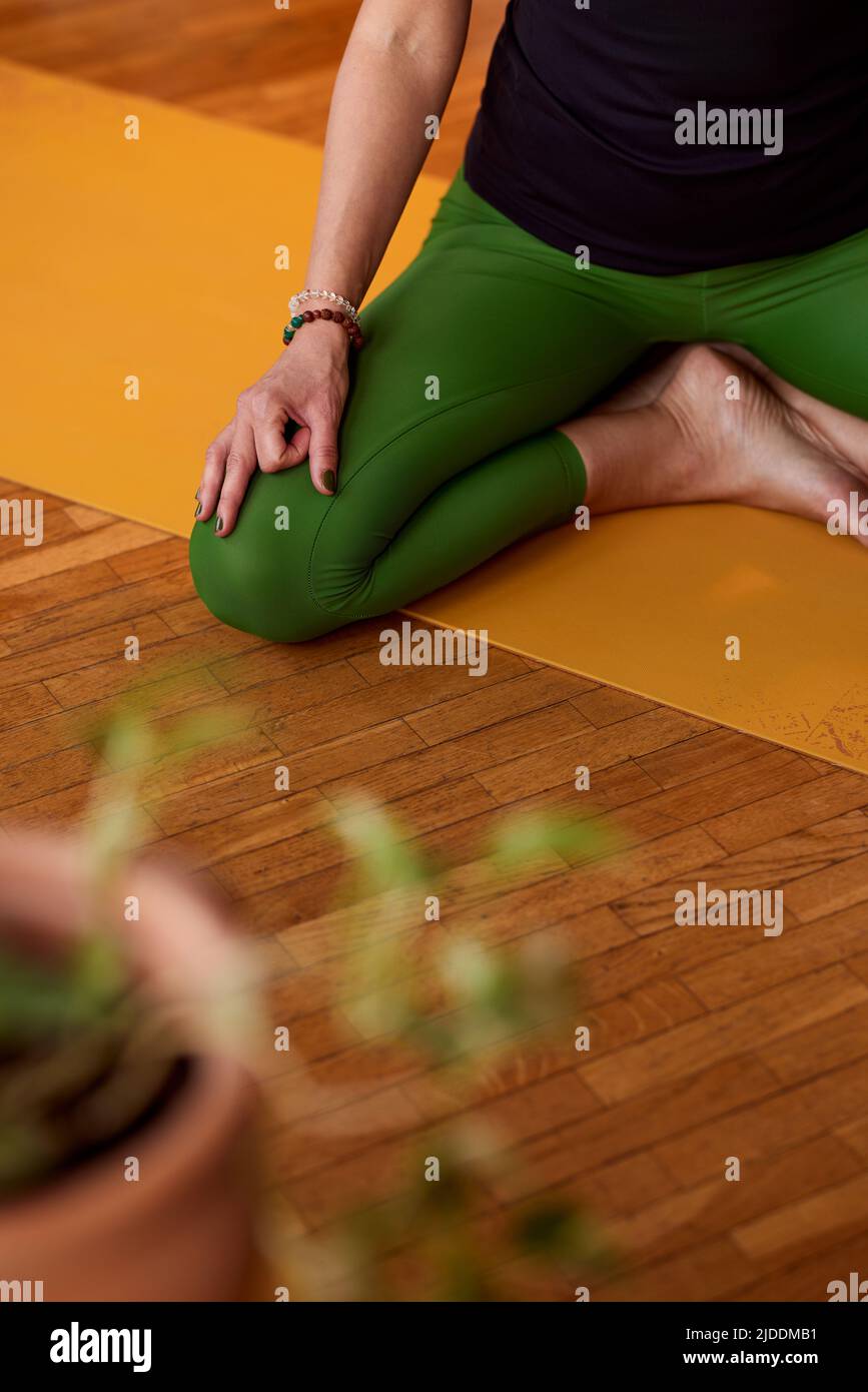 Nahaufnahme einer ruhigen Yogi-Frau mittleren Alters, die auf einer Yogamatte in einer Lotushaltung sitzt und meditiert. Eine Yogi-Frau, die zu Hause meditiert, übt zu Hause. Stockfoto