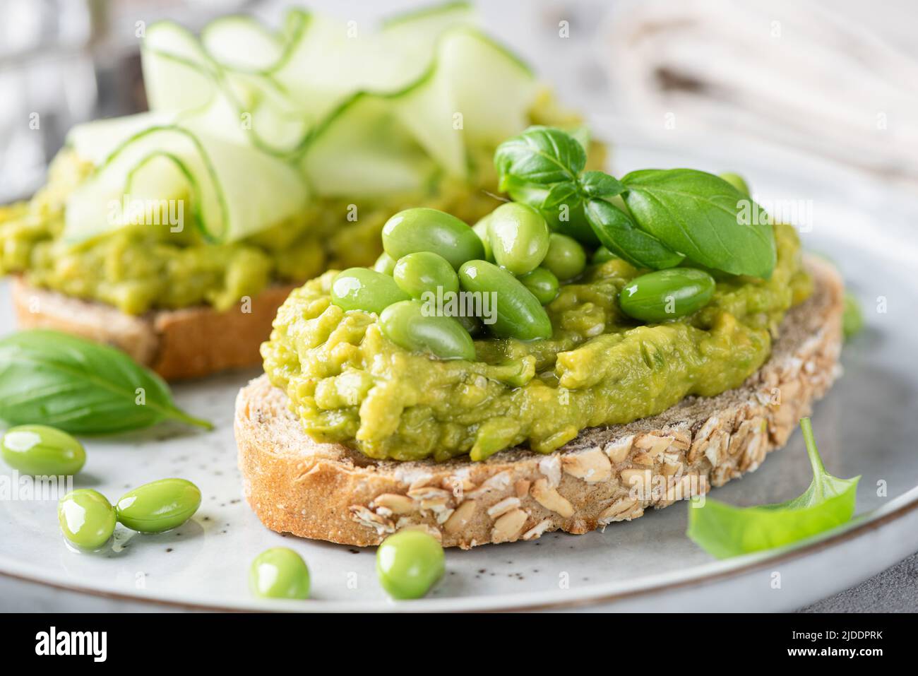 Frische grüne Avocado-Toasts mit Edamamabohnen und Gurkenaufschlägen. Sauberes Essen, gesundes veganes Lebensmittelkonzept. Nahaufnahme Stockfoto