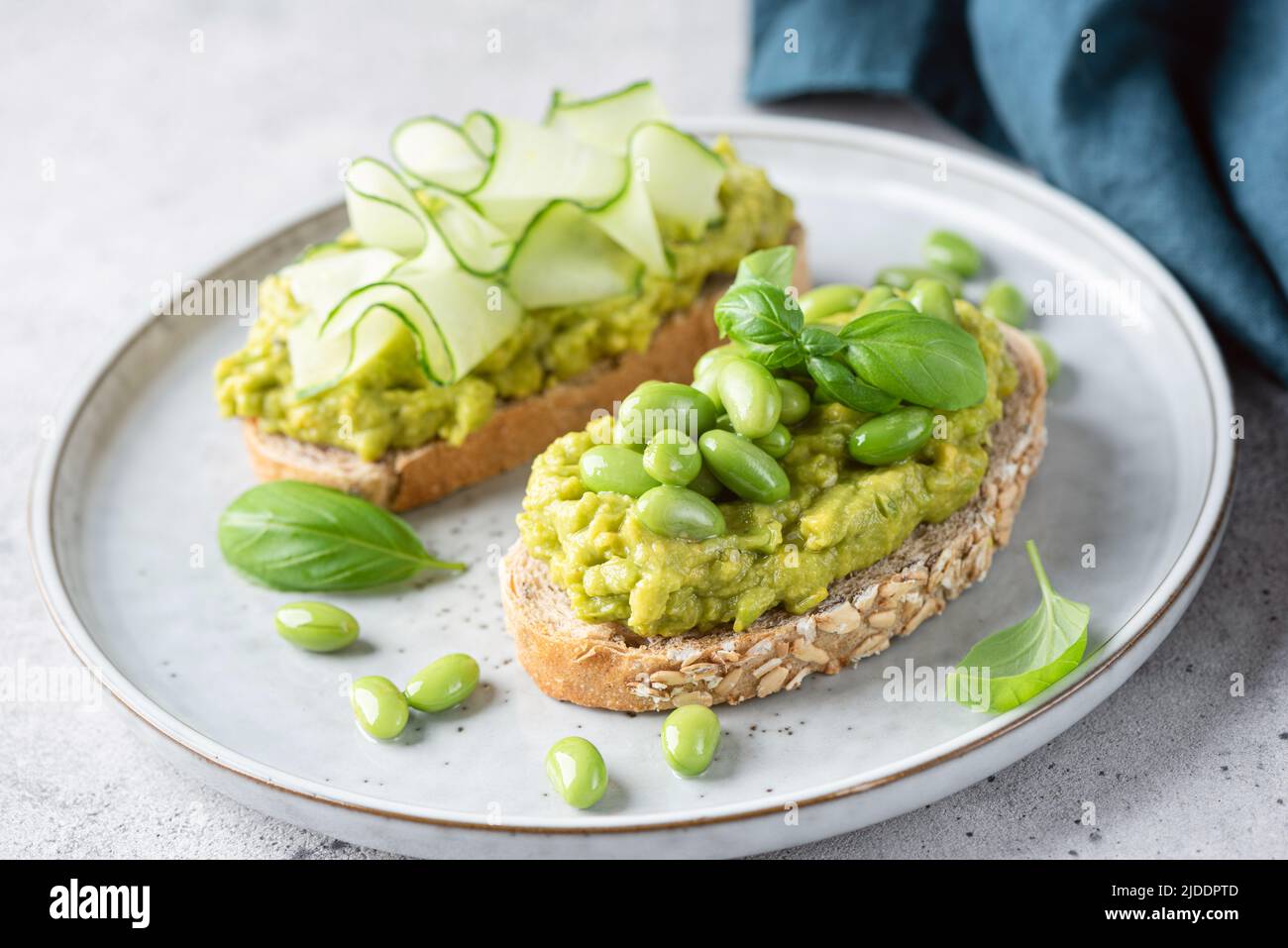 Avocado-Toasts mit Edamamabohnen, Gurkenscheiben und Basilikum. Gesundes grünes veganes Essen Stockfoto