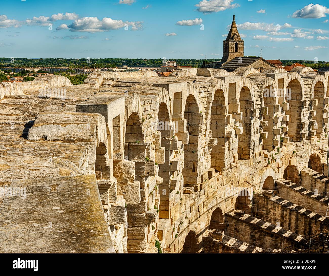 Der Blick über die Steinkolonnade, die die alte römische Arena von Arles umgibt, umfasst einige Kirchtürme aus der Stadt. Stockfoto