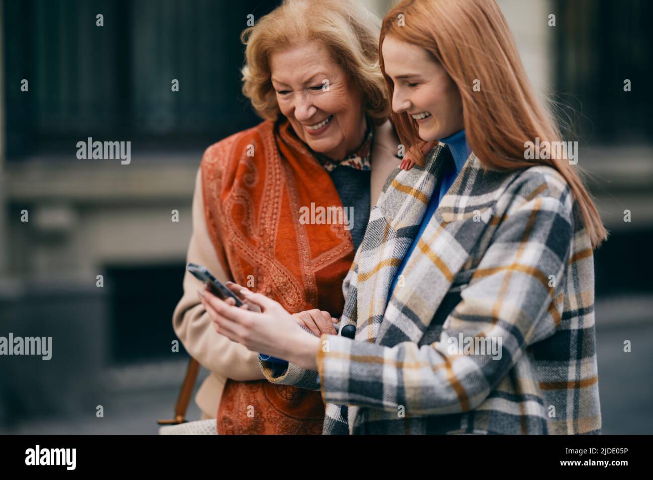 Eine Großmutter und ihr Enkelkind stehen auf der Straße und lesen Nachrichten am Telefon. Stockfoto