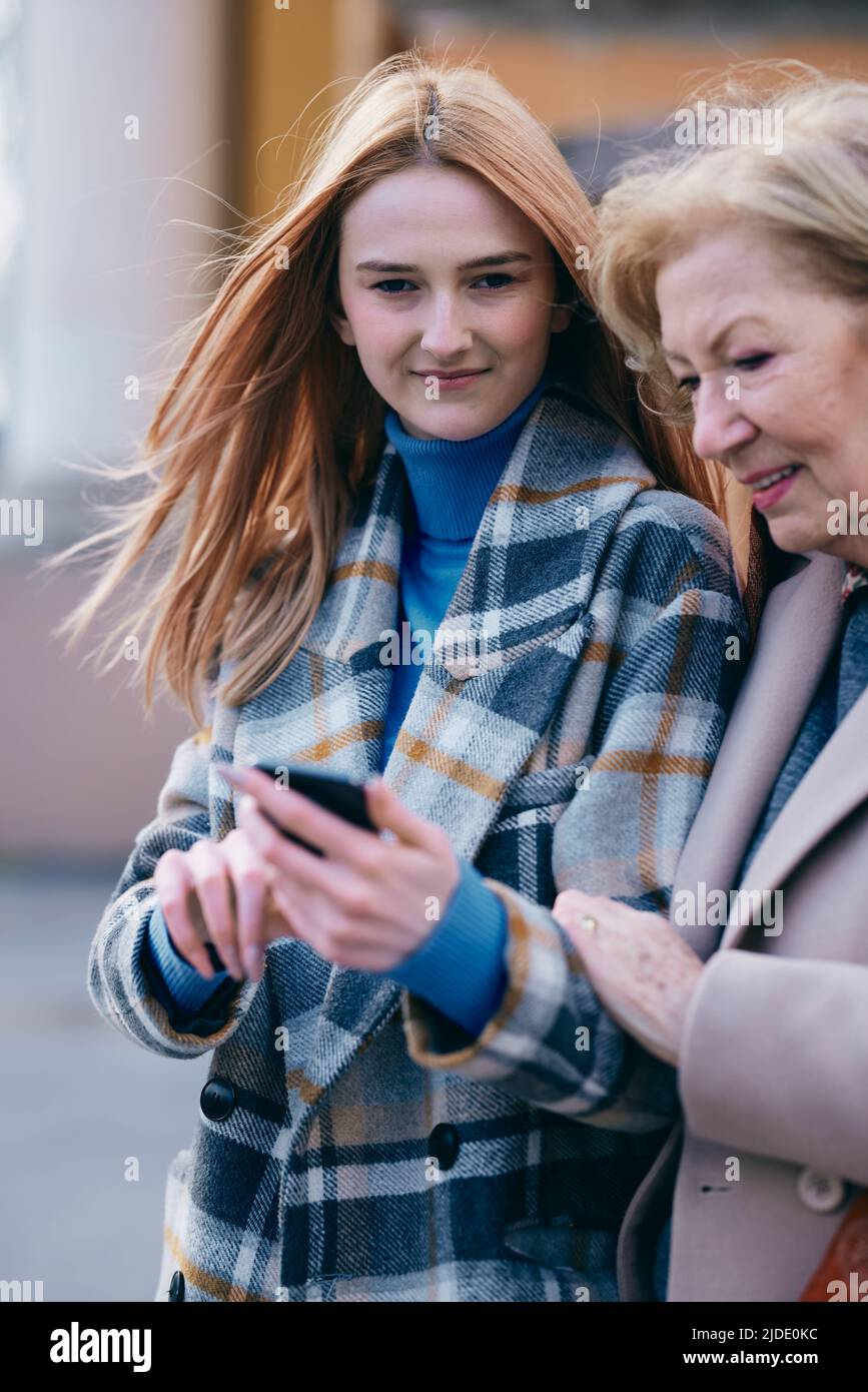 Eine Großmutter und ihr Enkelkind stehen auf der Straße und lesen Nachrichten am Telefon. Stockfoto