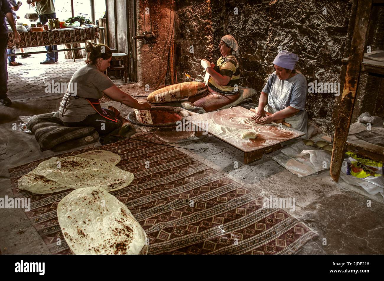 Lusakert, Armenien, 14. Mai 2022.: Eine Frau, die auf dem Boden sitzt, nimmt ein dünnes Blatt gebratener duftender Lavasch aus einem rotheißen Ofen auf den Boden. Stockfoto