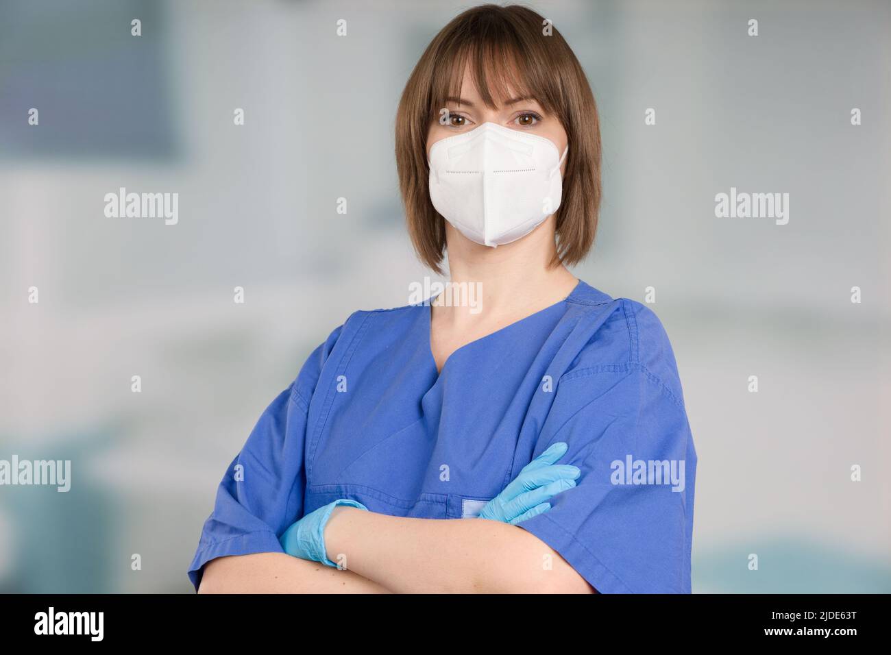 Porträt einer Ärztin oder einer Krankenschwester mit medizinischer Gesichtsmaske und medizinischen Handschuhen, die einen Operationsmantel vor einem Klinikraum tragen Stockfoto