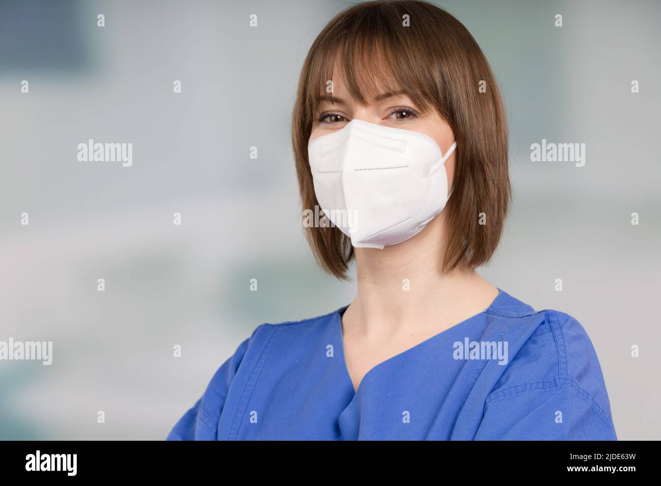 Porträt einer Ärztin oder einer Krankenschwester mit medizinischer Gesichtsmaske und medizinischen Handschuhen, die einen Operationsmantel vor einem Klinikraum tragen Stockfoto