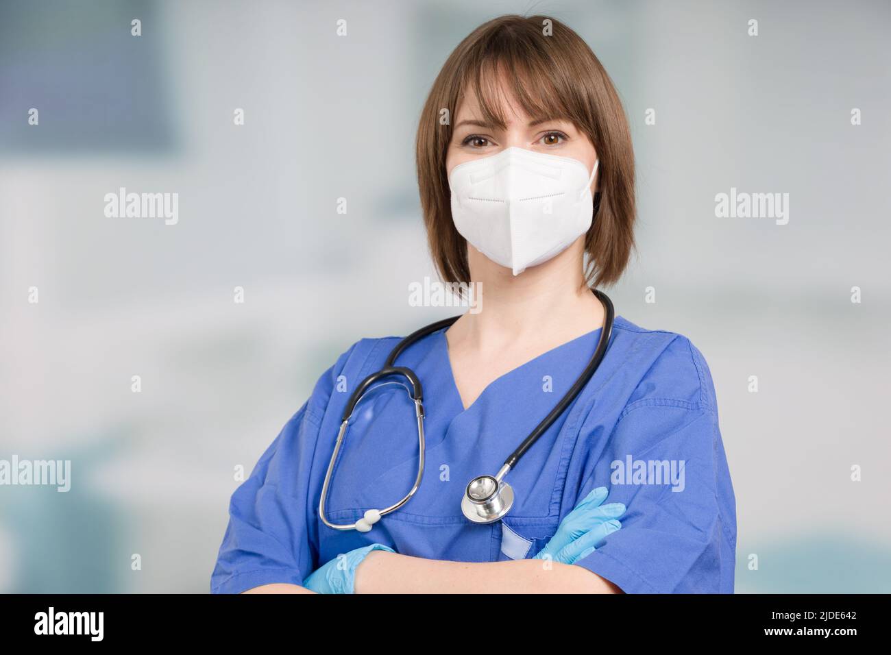 Porträt einer Ärztin oder einer Krankenschwester mit medizinischer Gesichtsmaske und medizinischen Handschuhen, die einen Operationsmantel vor einem Klinikraum tragen Stockfoto