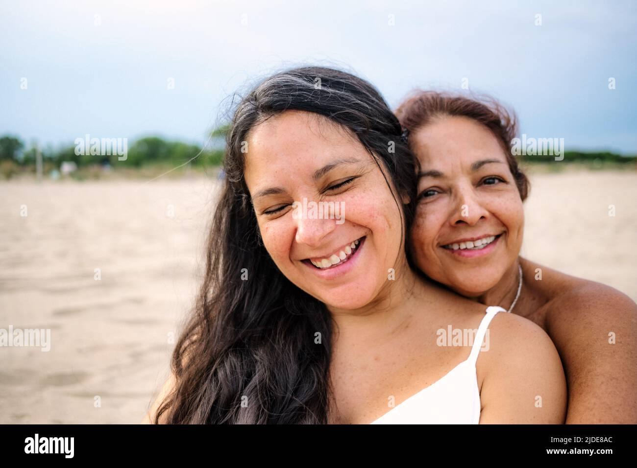 Nahaufnahme der alten Mutter und der schwanger erwachsenen Tochter werden gesehen umarmen und lächeln an einem Strand mit weißem Kleid Stockfoto
