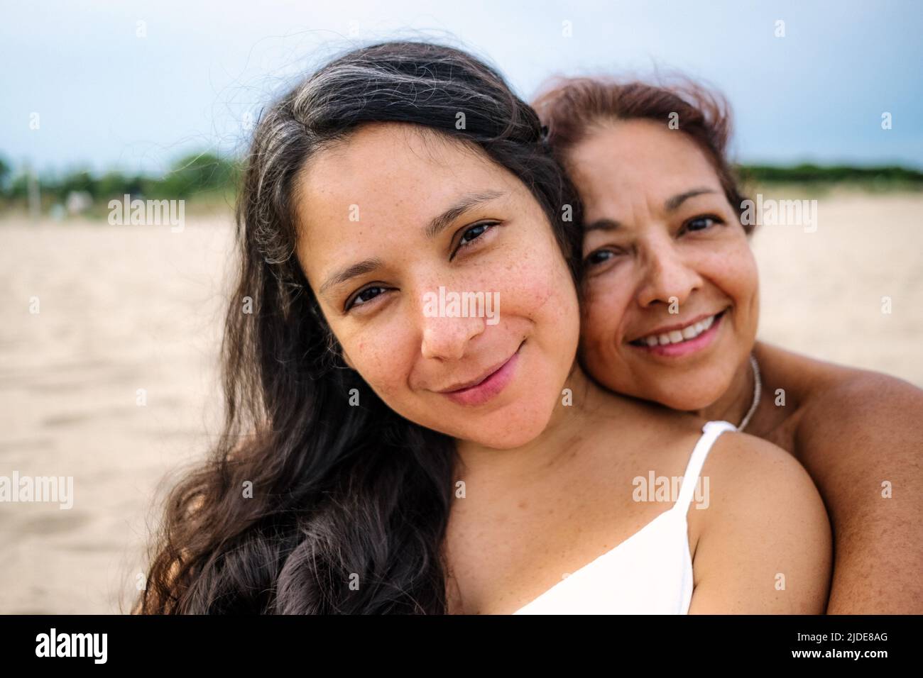 Nahaufnahme der alten Mutter und der schwanger erwachsenen Tochter werden gesehen umarmen und lächeln an einem Strand mit weißem Kleid Stockfoto