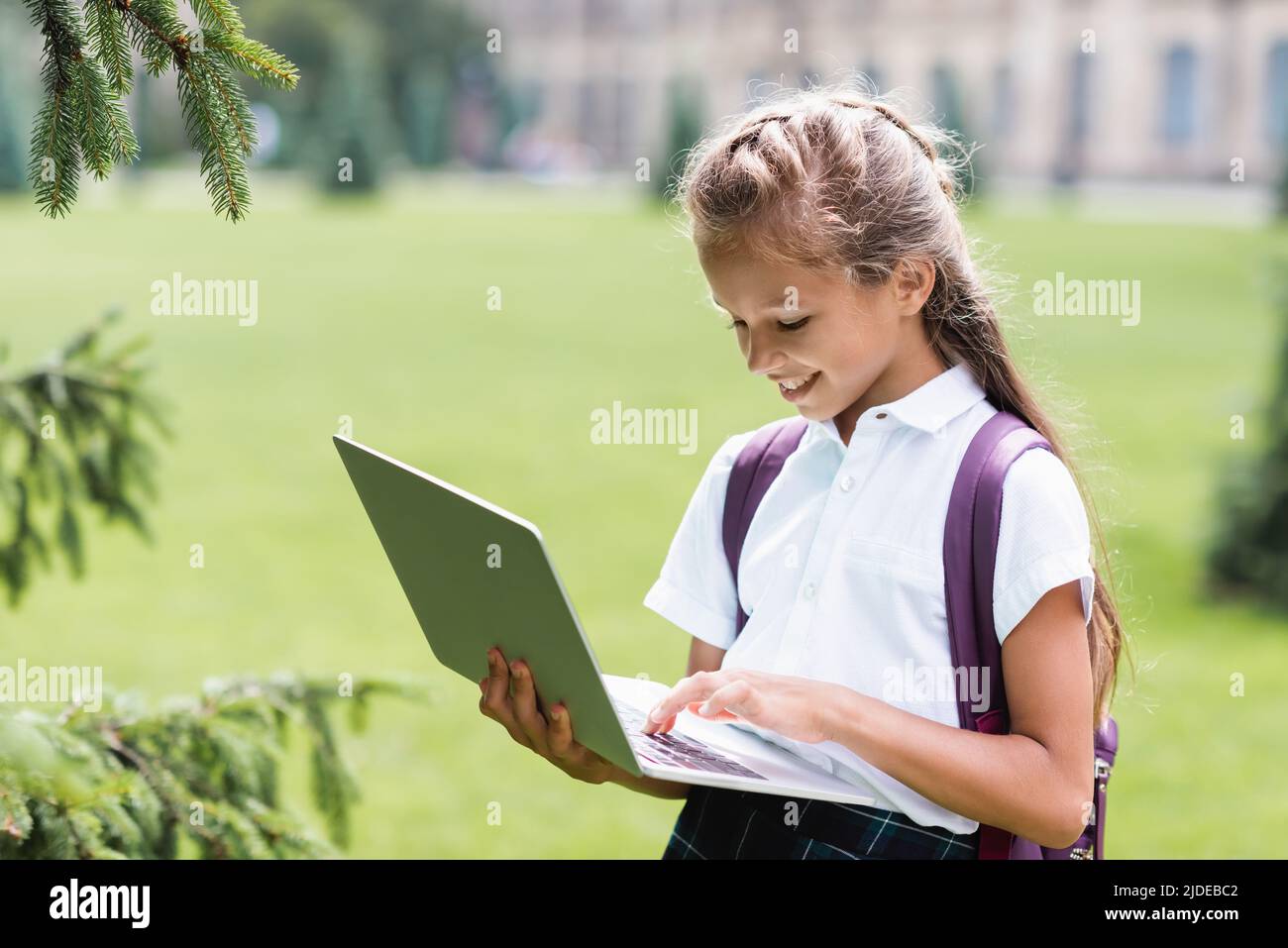 Lächelndes Schulmädchen mit Rucksack mit Laptop im Freien Stockfoto