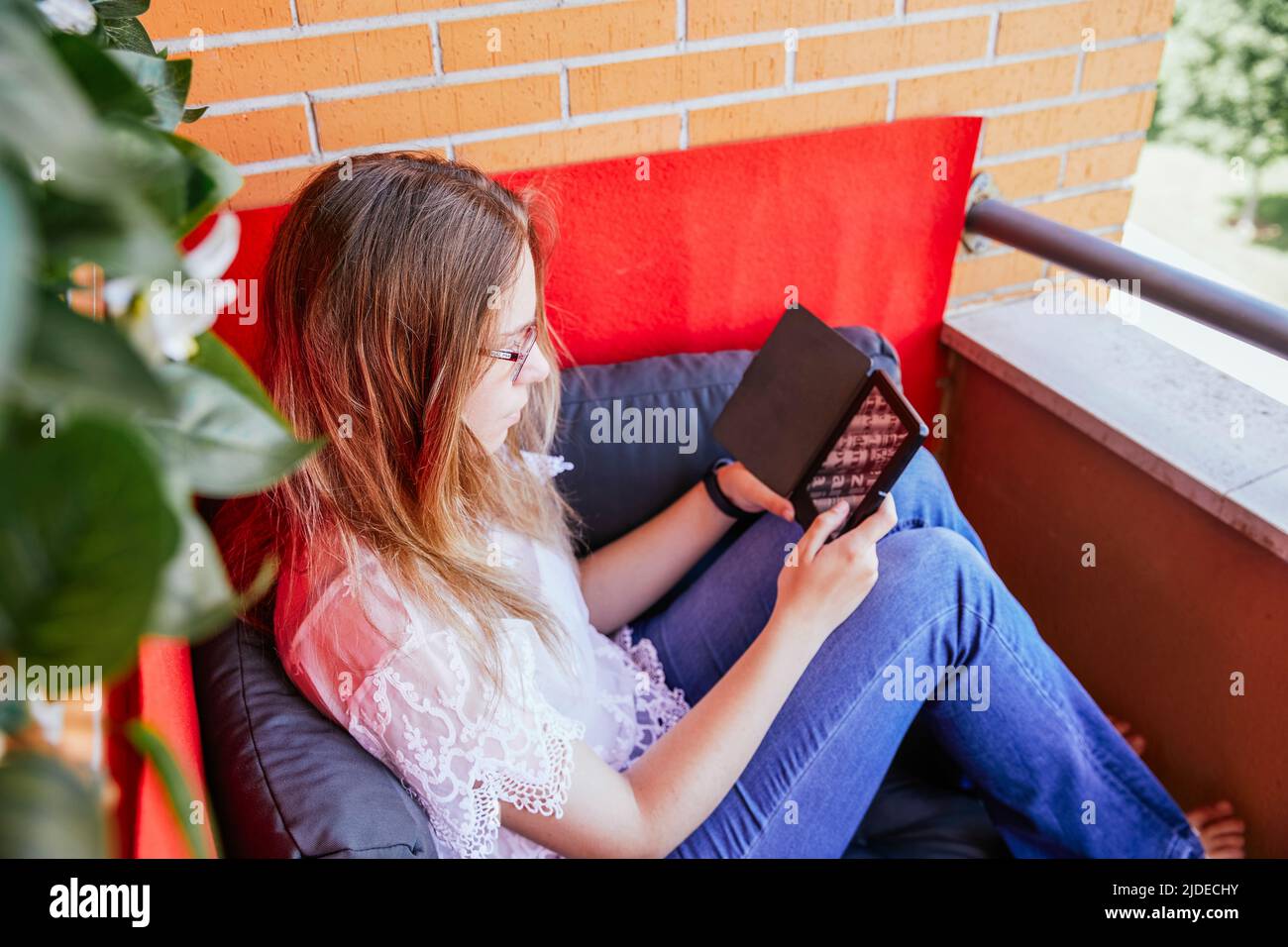 Draufsicht auf ein Mädchen, das mit ihrem eBook auf der Terrasse ihres Hauses liest. Stockfoto