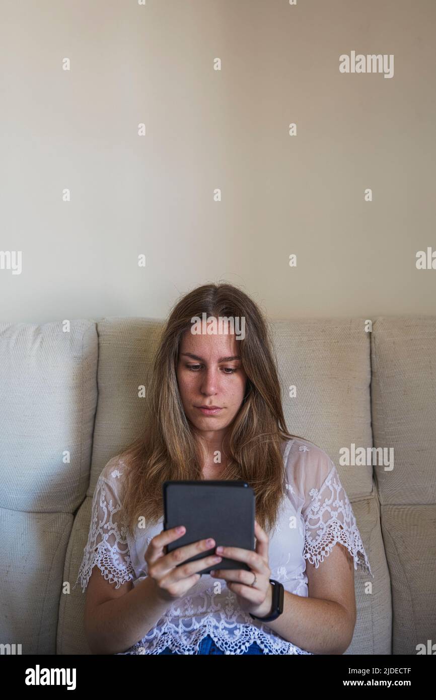 Vertikales Bild einer jungen Frau mit ihrem eBook auf einem Sofa Stockfoto