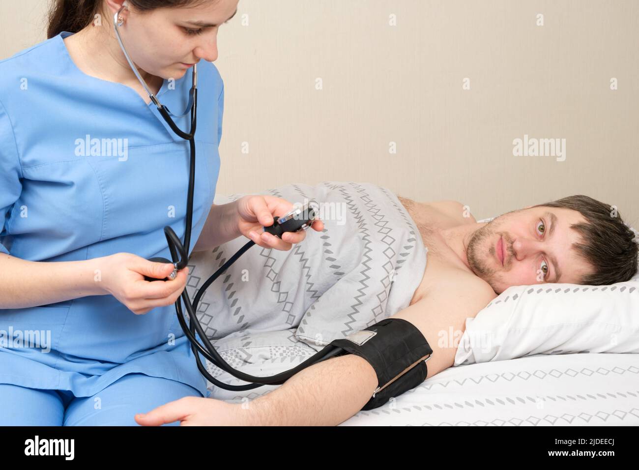Der Arzt misst den Blutdruck eines jungen 30-jährigen Mannes, der im Bett liegt. Erkrankungen des Herzens und der Blutgefäße beim Menschen, mechanische Tonomete Stockfoto
