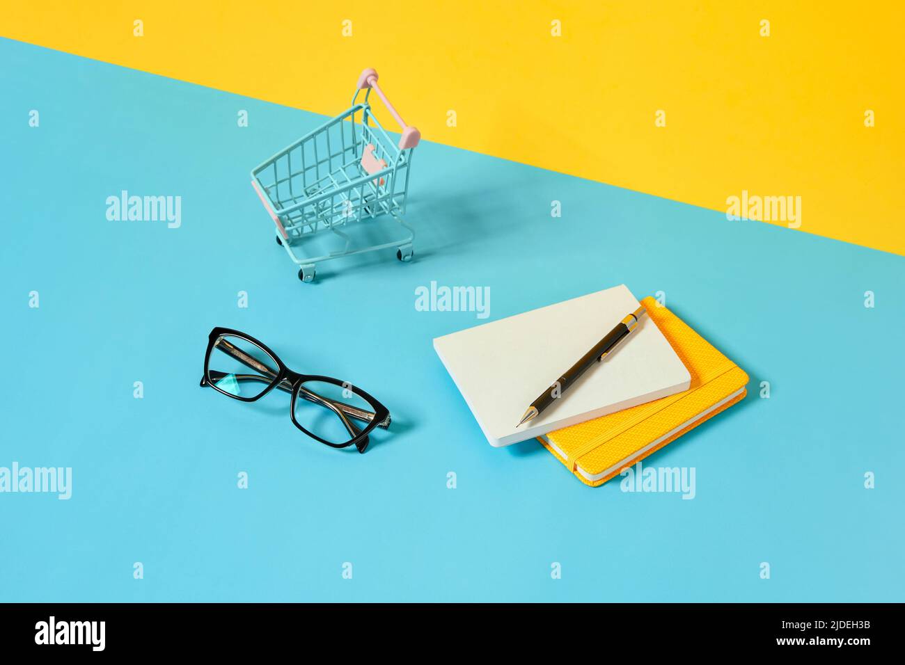 Smartphone, Schreibwaren, Brille und Einkaufswagen über blauem Tisch. Stockfoto