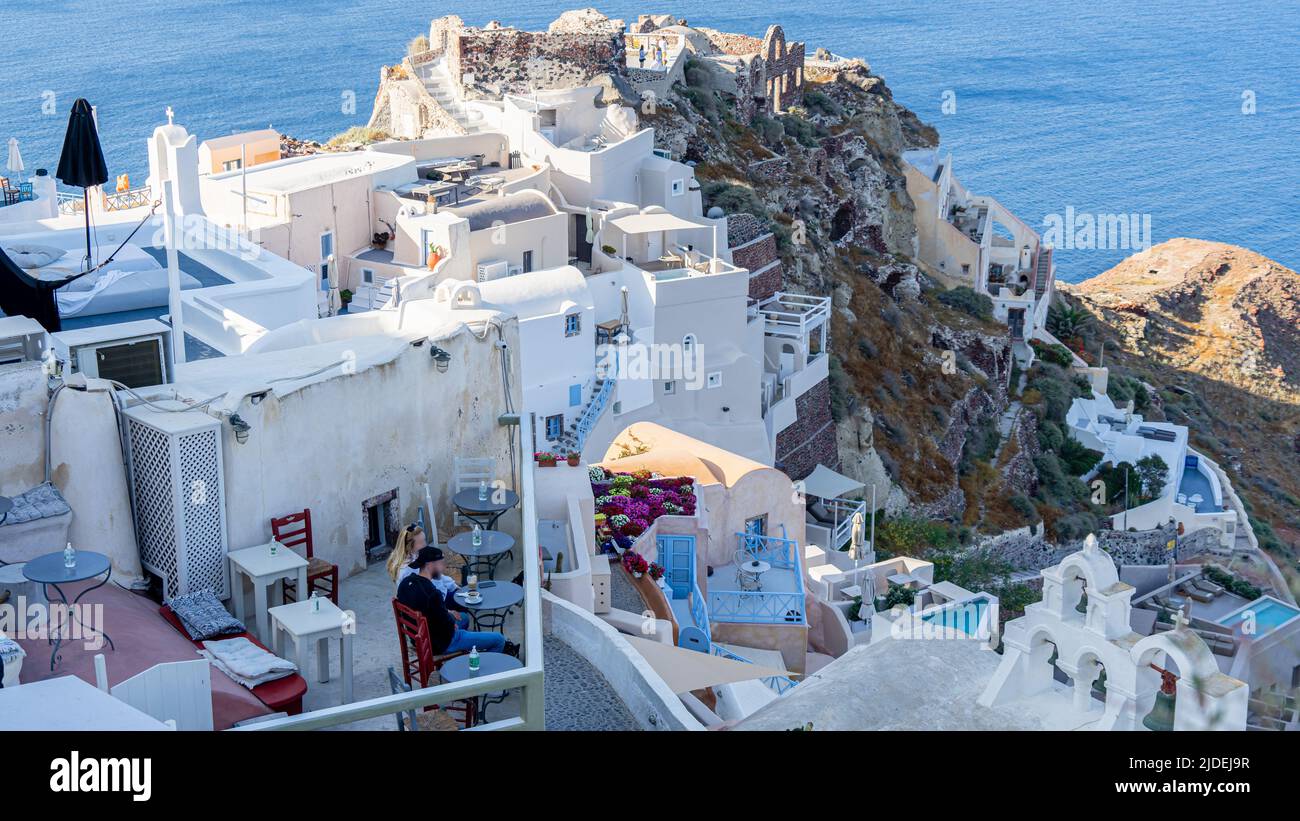 Ein Blick auf die steilen Terrassen der ikonischen Oia auf der Insel Santorini mit den Ruinen der Burg Agios Nikolaos im Hintergrund Stockfoto