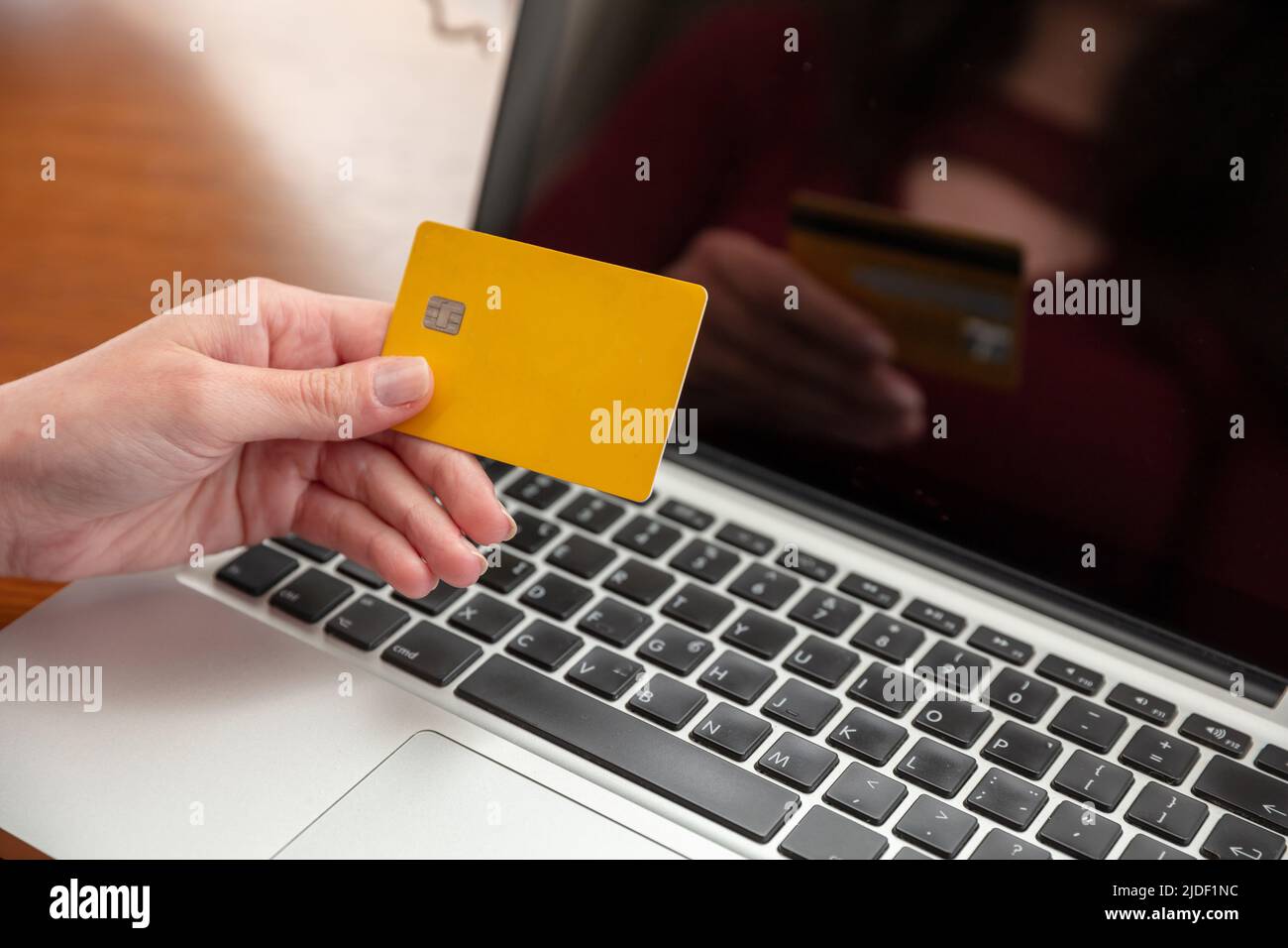 Online-Shopping, Kreditkartenzahlung. Weibliche Hände halten leere gelbe Plastikkarte und mit Computer-Laptop, Nahaufnahme, Kopierraum. Stockfoto