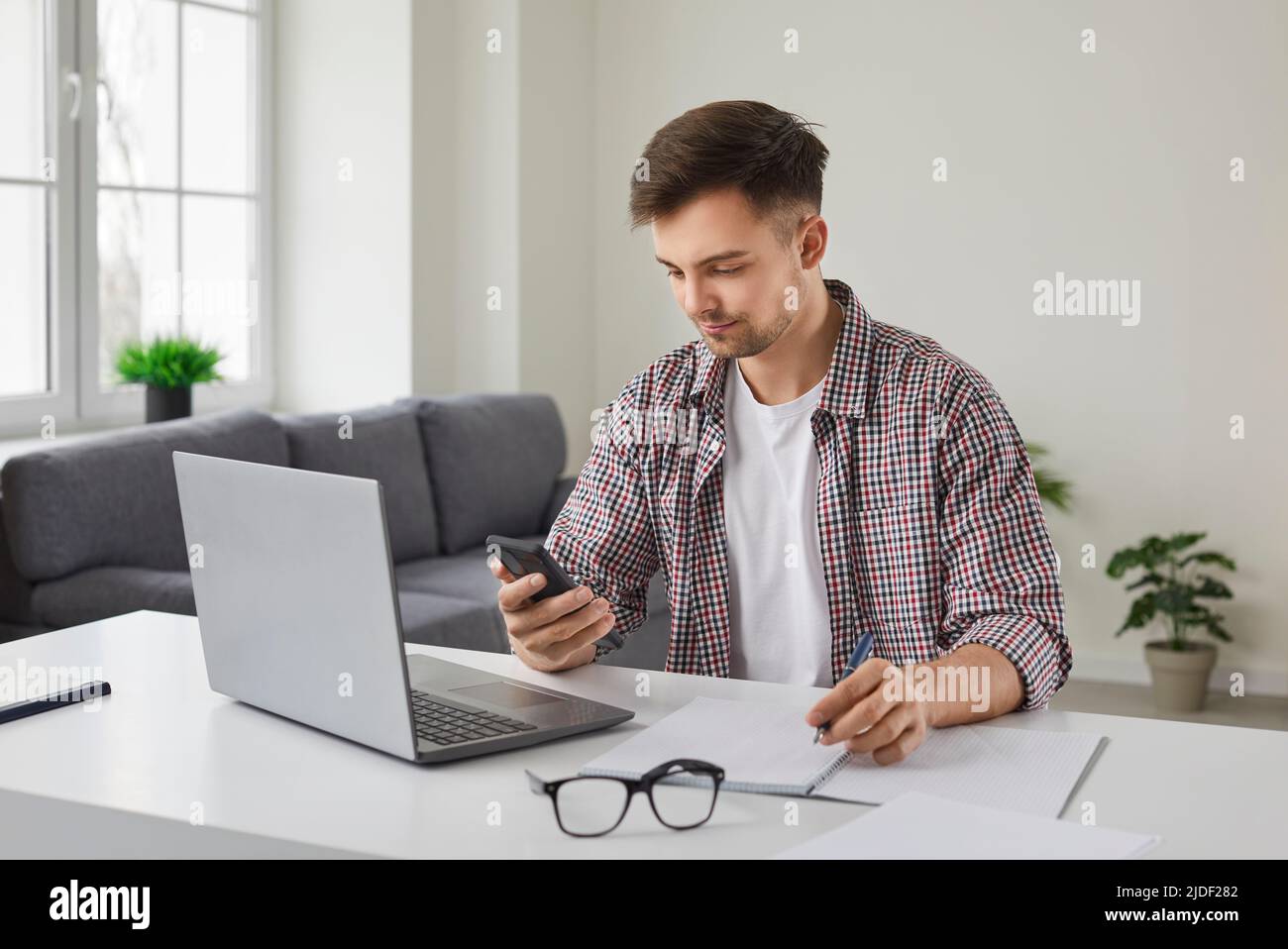 Junger Geschäftsmann, der mit einem Mobiltelefon am Schreibtisch mit einem Laptop sitzt Stockfoto