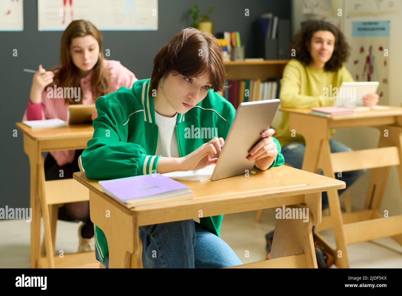 Jugendliche Schülerin in Casualwear, die auf den Tablet-Bildschirm schaut, während sie online durch die Tipps zum Unterricht unter ihren Klassenkameraden scrollt Stockfoto