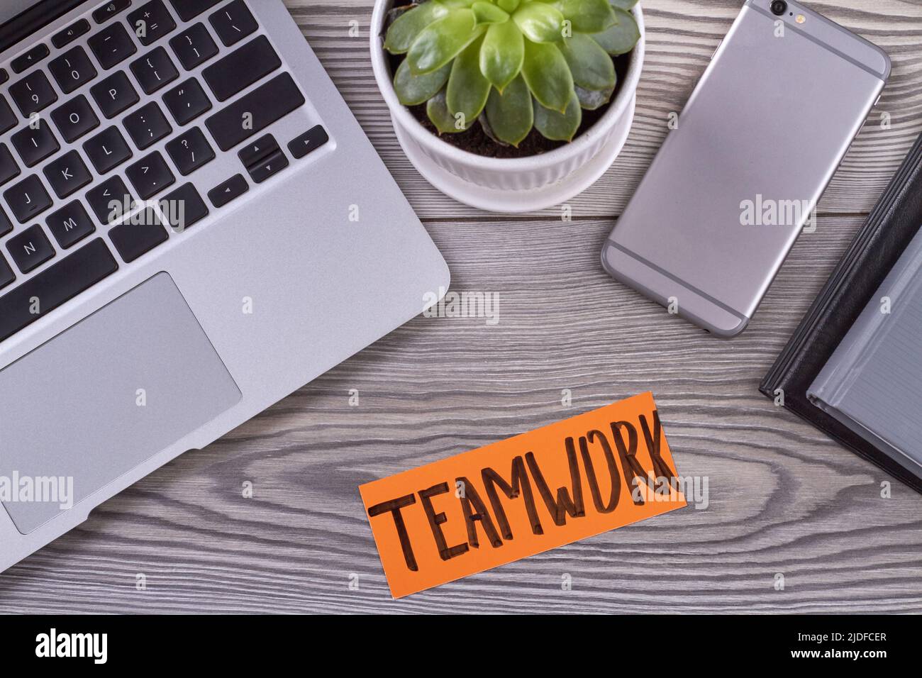 Digitale Geräte von oben mit Blumentopf auf dem Schreibtisch. Teamwork-Wort auf dem Papier. Stockfoto
