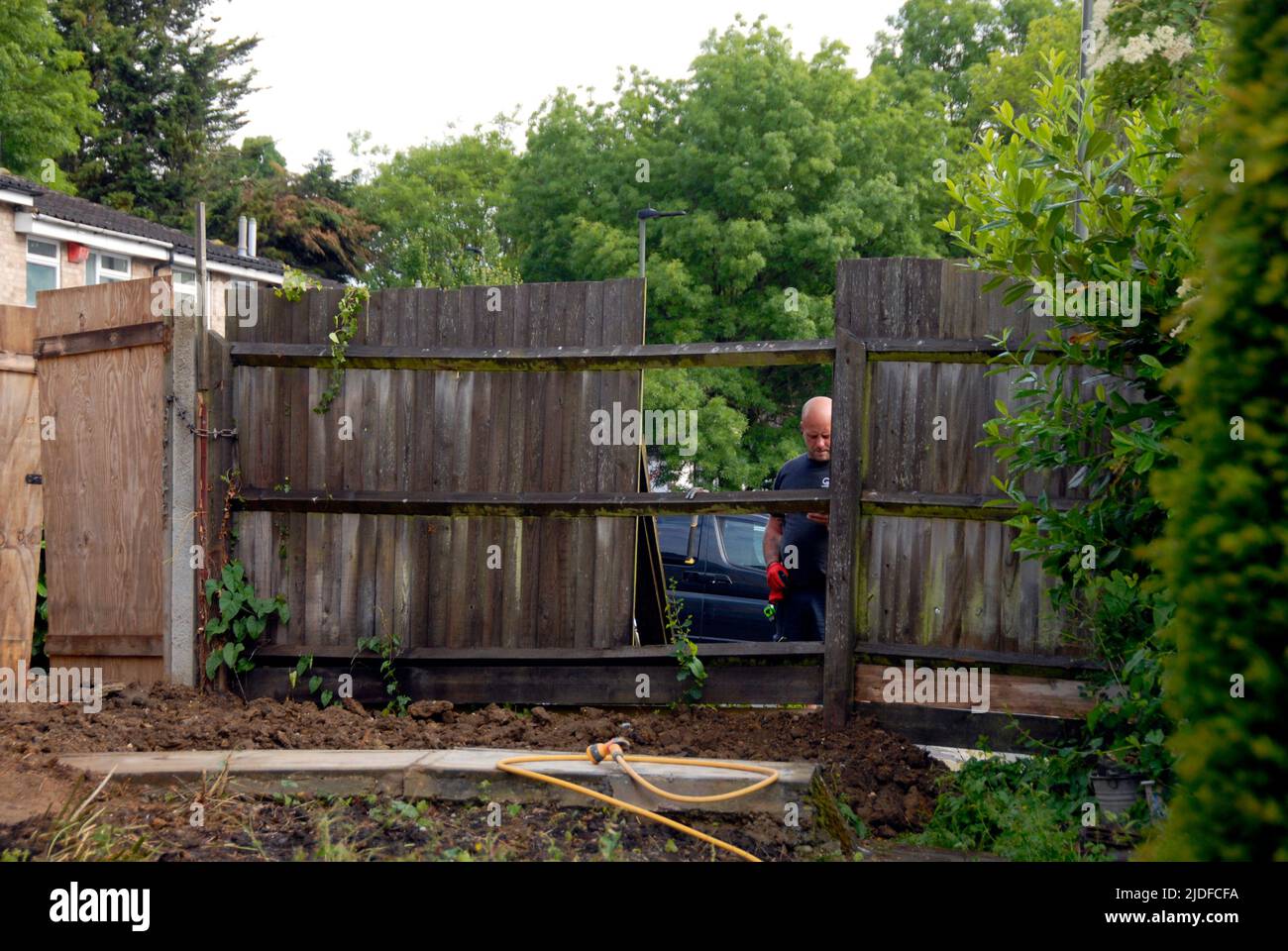 Arbeiter fangen an, alten häuslichen Gartenzaun auseinander zu nehmen, bevor er durch einen neuen Zaun ersetzt wird Stockfoto
